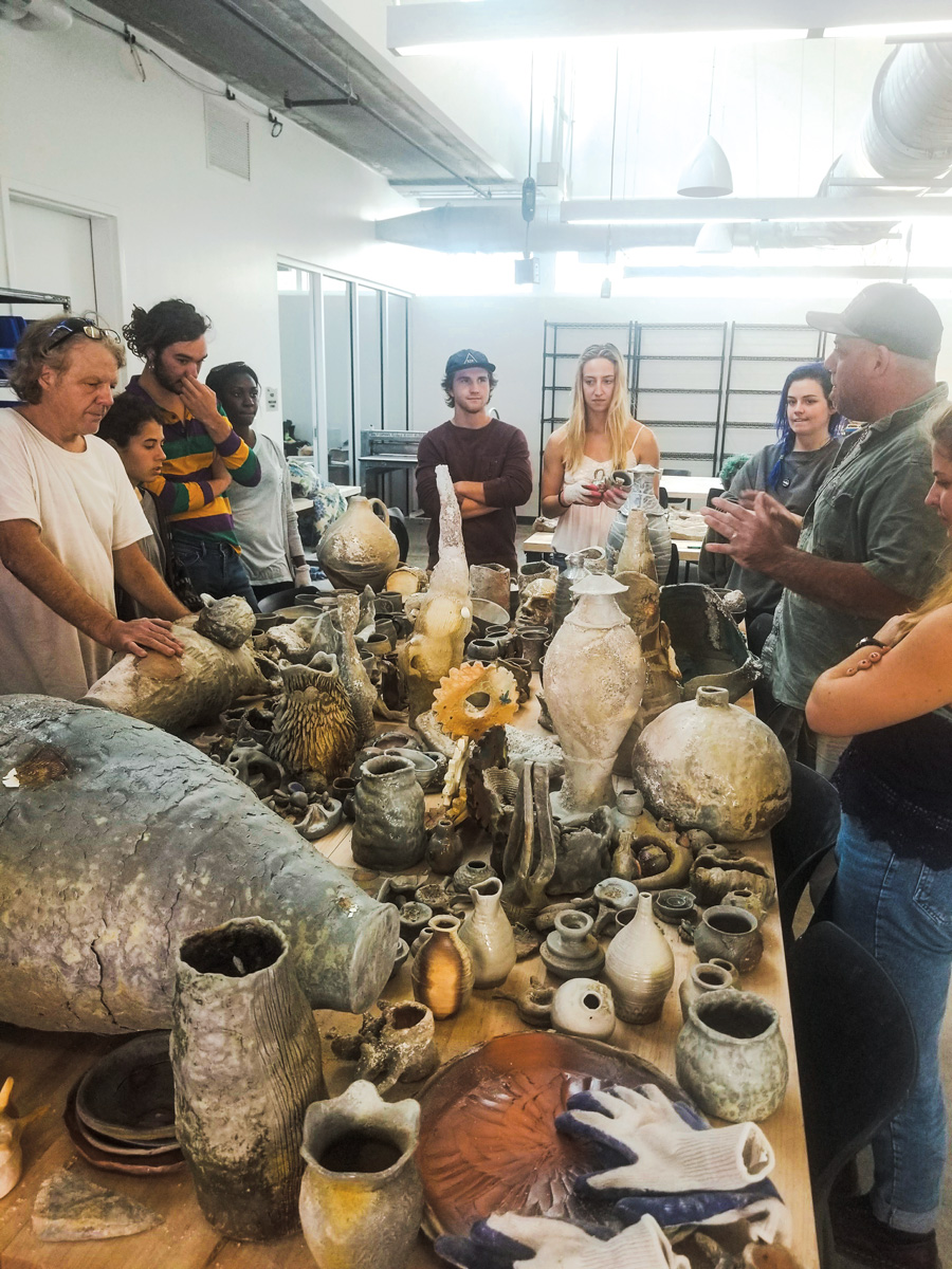 students stand around a table looking at a table of ceramics