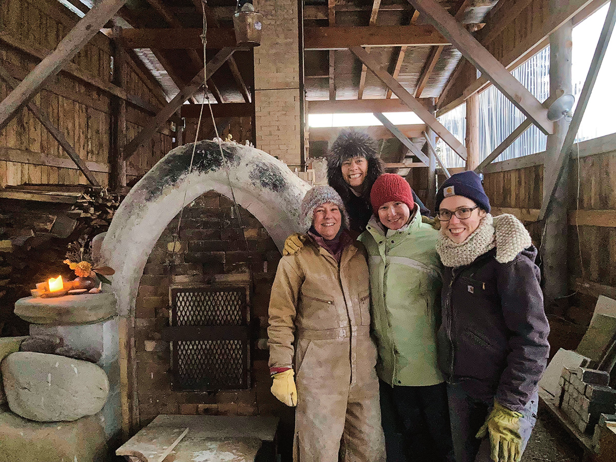 four people huddle together and smile next to a kiln