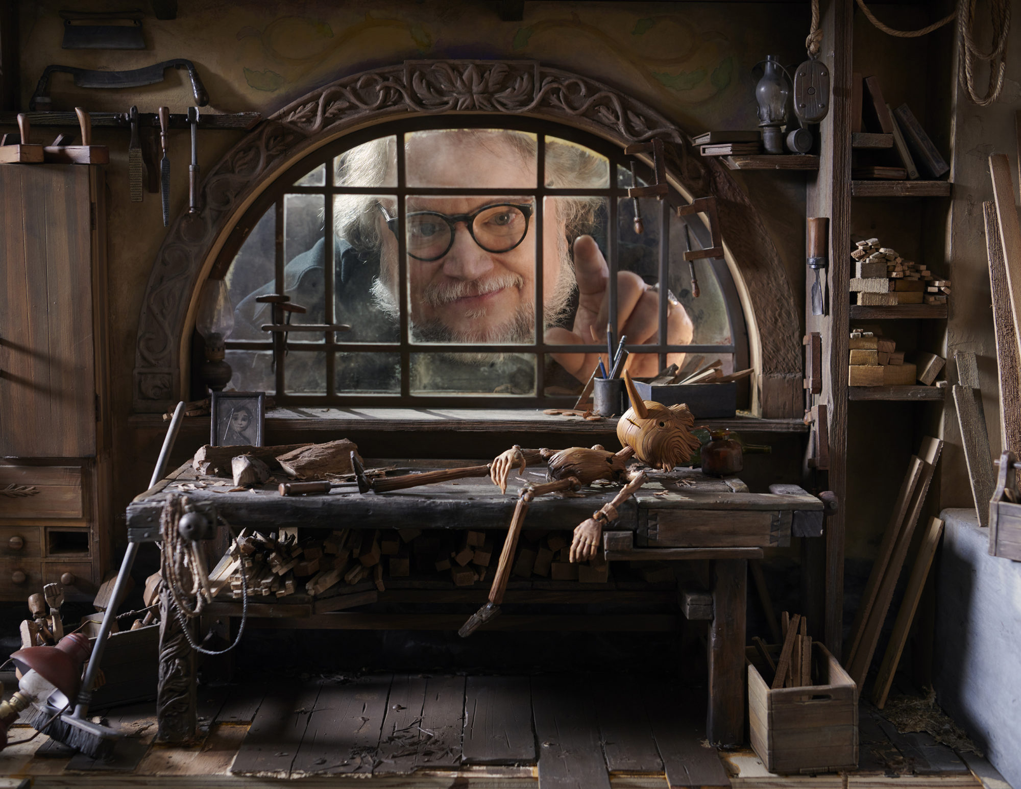 Man with beard and glasses peering into the set of a miniature claymation Pinocchio